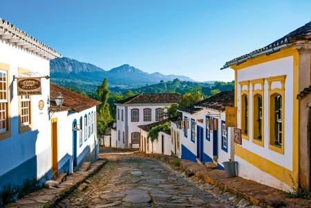 Charming colonial street in Tiradentes, Brazil, with traditional white and colorful buildings, cobblestone streets and mountain scenery in the background on a sunny day.