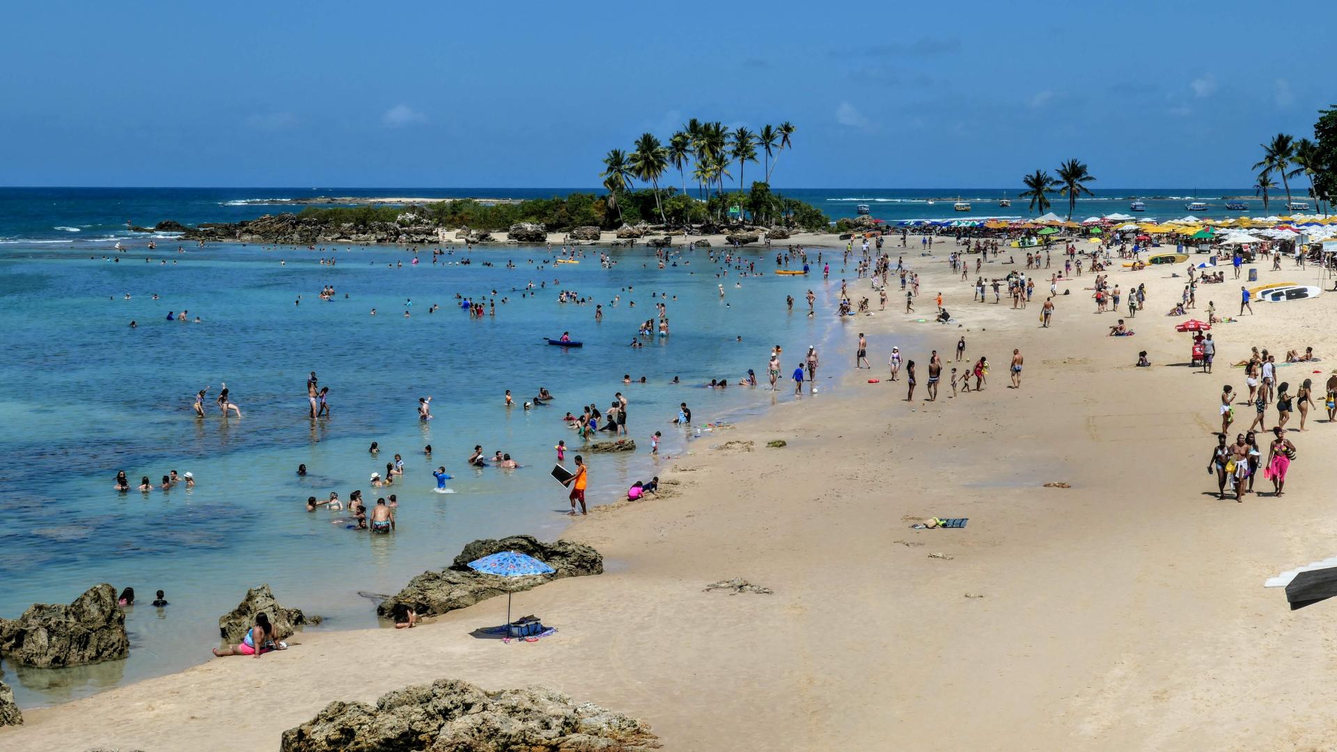 Beach in Morro de São Paulo, Brazil, with lots of locals in the turquoise blue water and under palm trees.