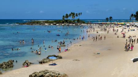 Beach in Morro de São Paulo, Brazil, with lots of locals in the turquoise blue water and under palm trees.