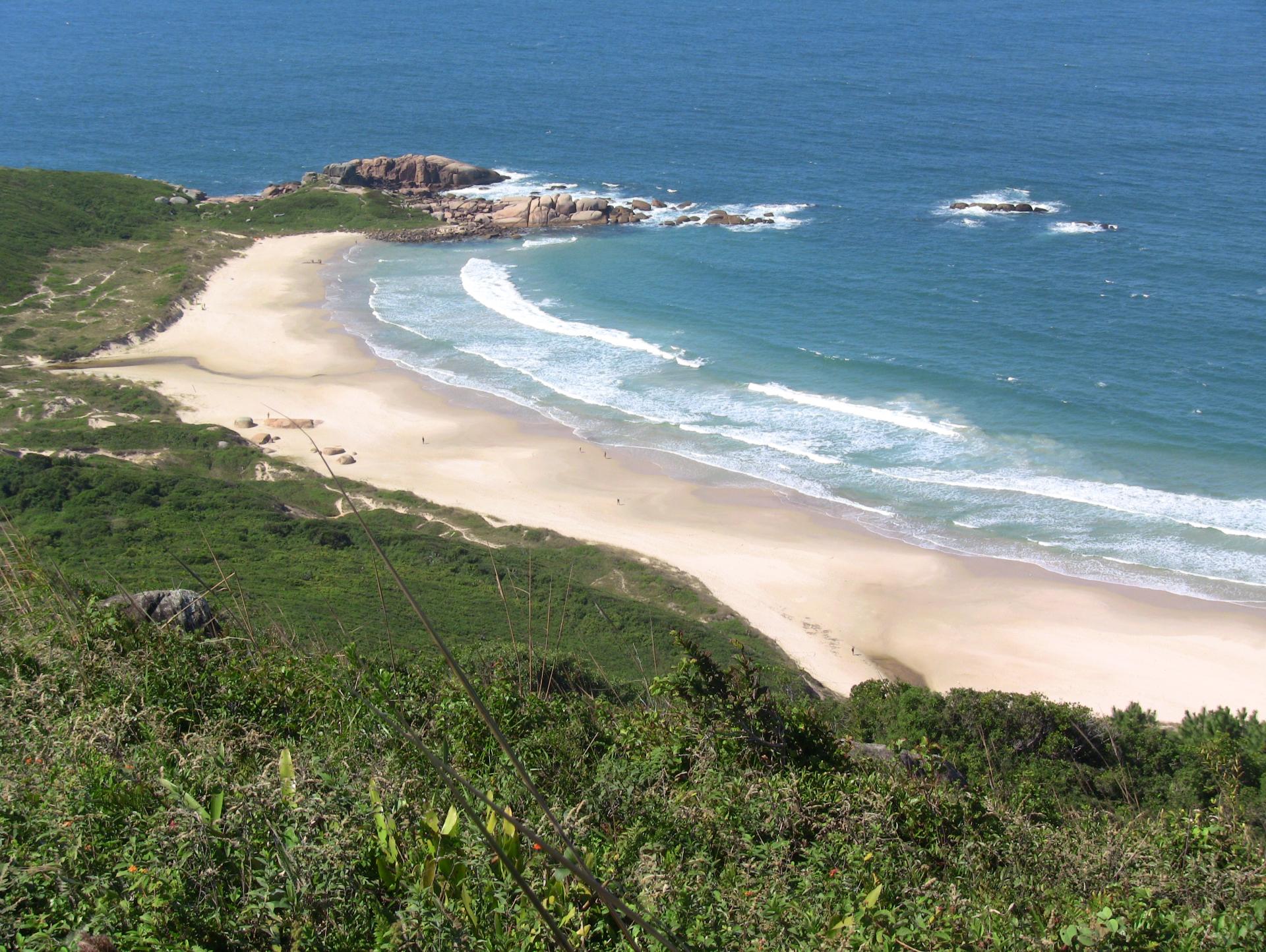 Aerial view of the secluded Lagoinha do Leste beach in Florianópolis, Brazil. Fine white sand, Atlantic Ocean waves, and lush green hills in the background.