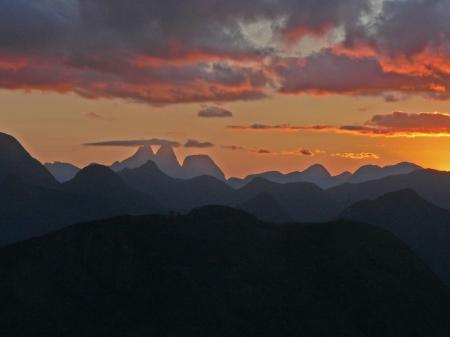 Stunning view from the Itororó Eco Lodge of the mountain silhouettes in Três Picos National Park at sunset, with a dramatic sky in shades of red and orange.