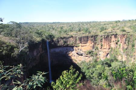 A breathtaking view of the Véu de Noiva waterfall cascading down a high cliff, surrounded by lush greenery and rocky landscapes in Chapada dos Guimarães National Park, Brazil